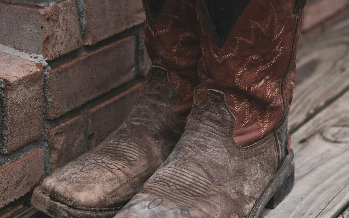 A worn pair of brown boots resting beside a brick wall.