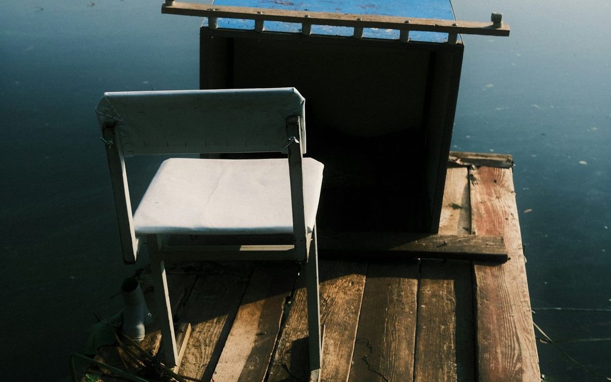 An empty chair on a weathered wooden dock beside still water.