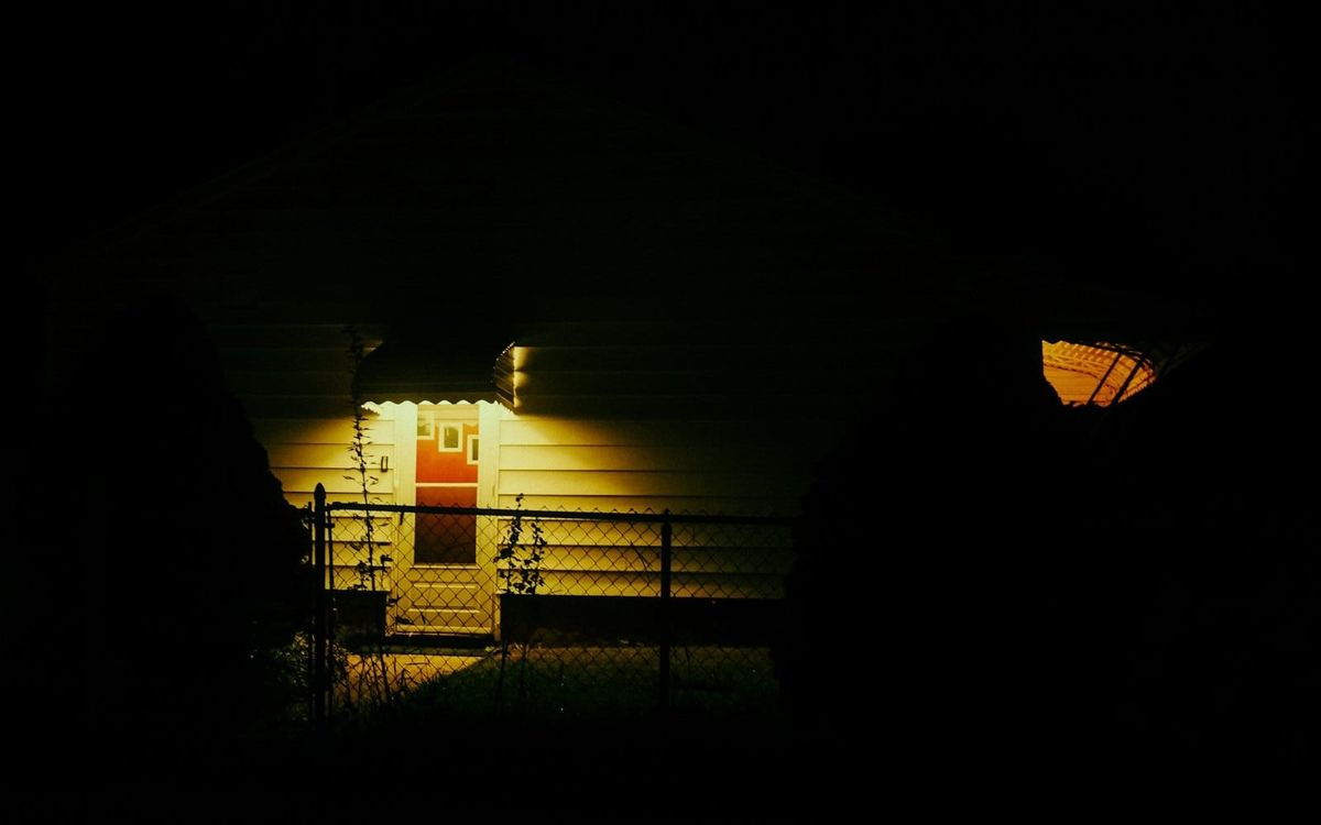 A porch light illuminates the front door of a small house after dark