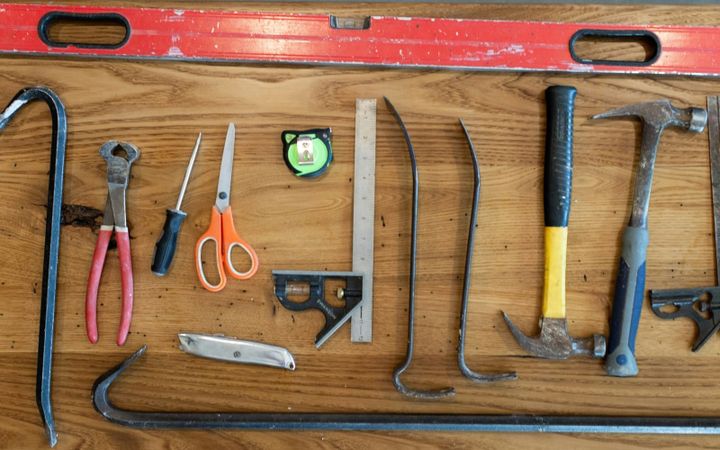 Basic hand tools and fasteners arranged on a worn wooden workbench.