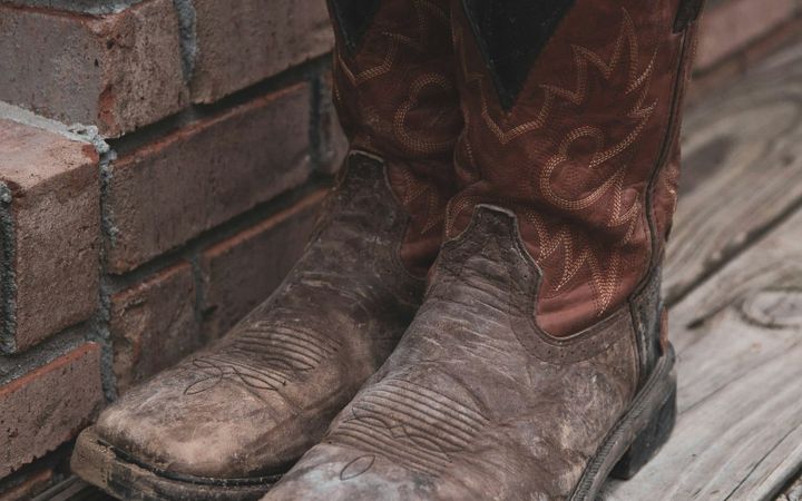 A worn pair of brown boots resting beside a brick wall.