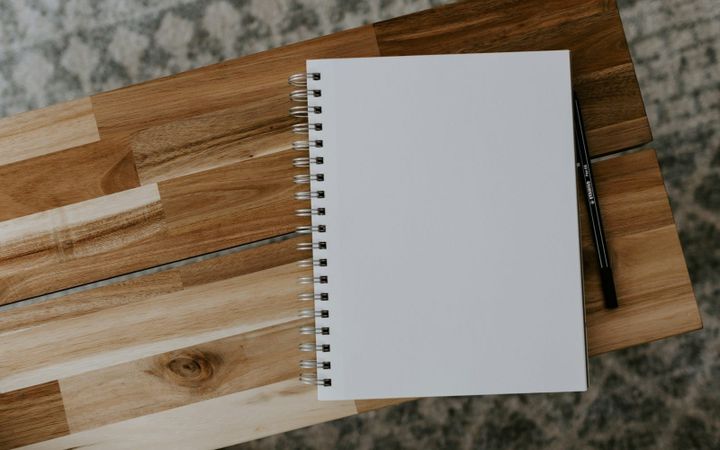 A blank spiral notebook and pen on a simple wooden table.