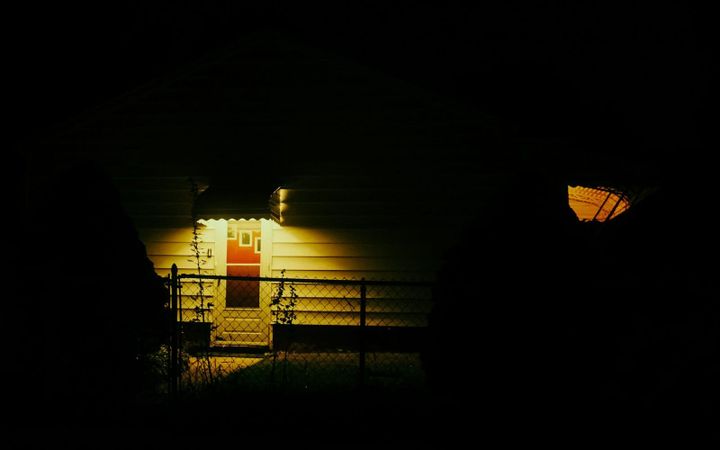 A porch light illuminates the front door of a small house after dark