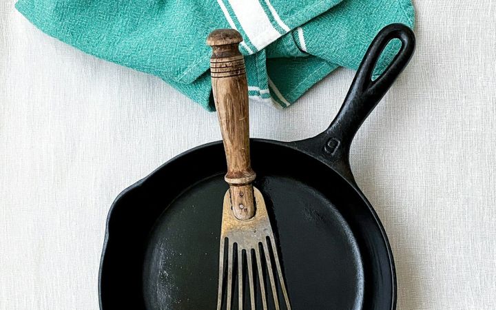 A cast iron skillet and well-used metal spatula beside a kitchen towel