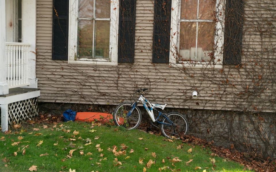 A bicycle resting beside a weathered wooden house in a quiet yard.