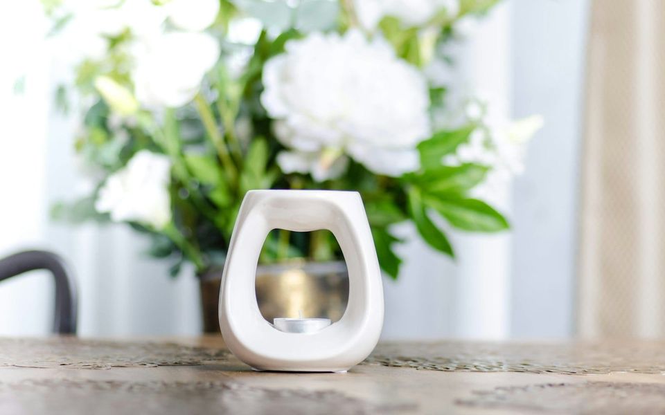 A small white ceramic fragrance burner resting on a wooden surface.