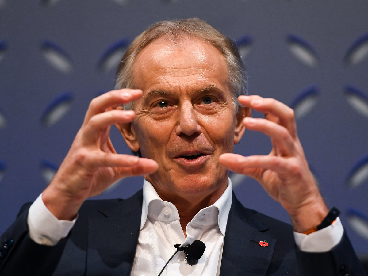 A picture of Tony Blair in a navy suit, gesturing with both hands in front of his face.