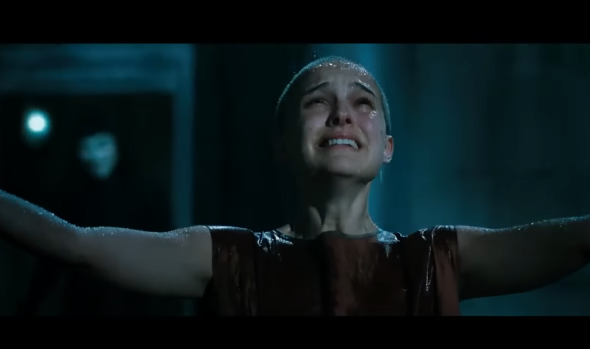 A screengrab from the movie V for Vendetta where Evey stands in the rain, arms outstretched gazing up at the sky. V stands behind her out of focus