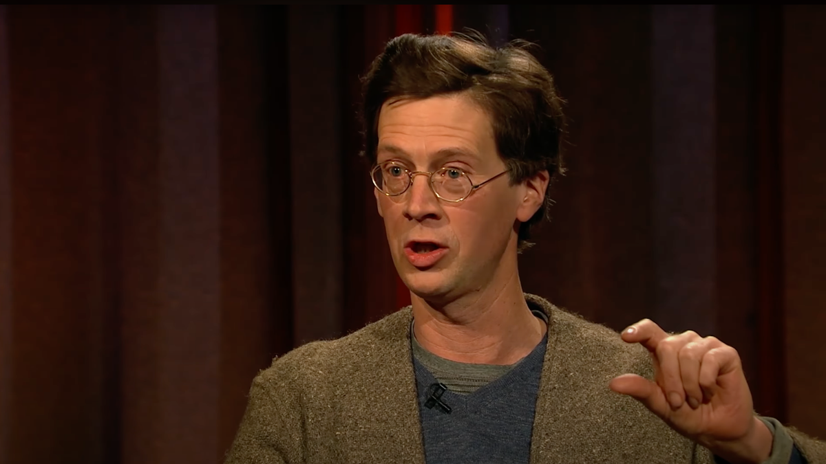 Manchán Magan is a white man with brown short hair and round spectacles.