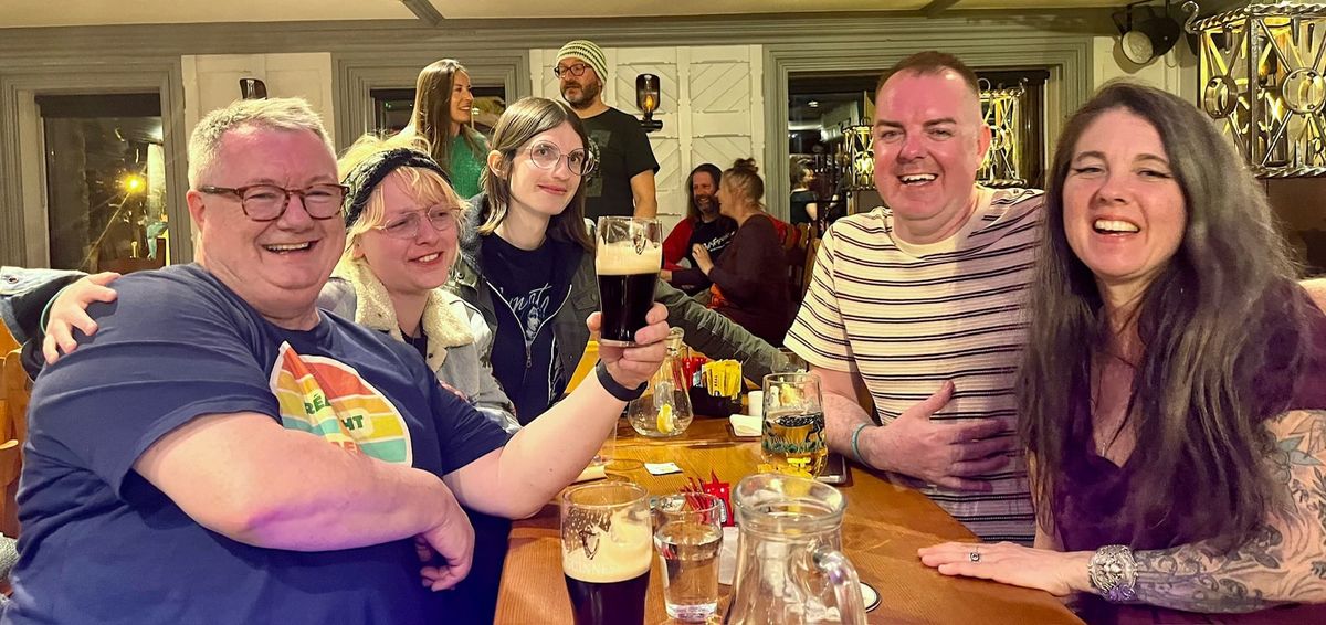 A group of people sit smiling as one holds a pint of guinness with a successfully split G