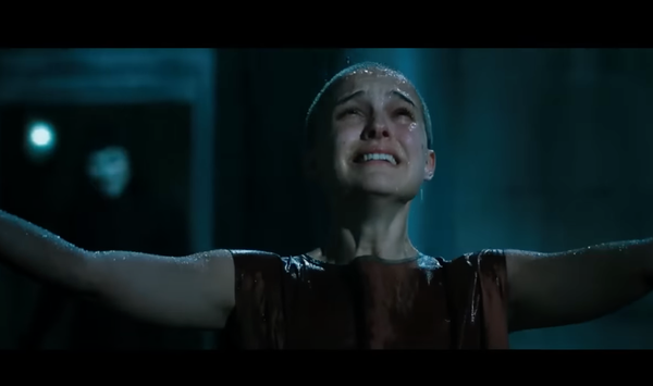 A screengrab from the movie V for Vendetta where Evey stands in the rain, arms outstretched gazing up at the sky. V stands behind her out of focus