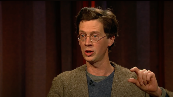 Manchán Magan is a white man with brown short hair and round spectacles.