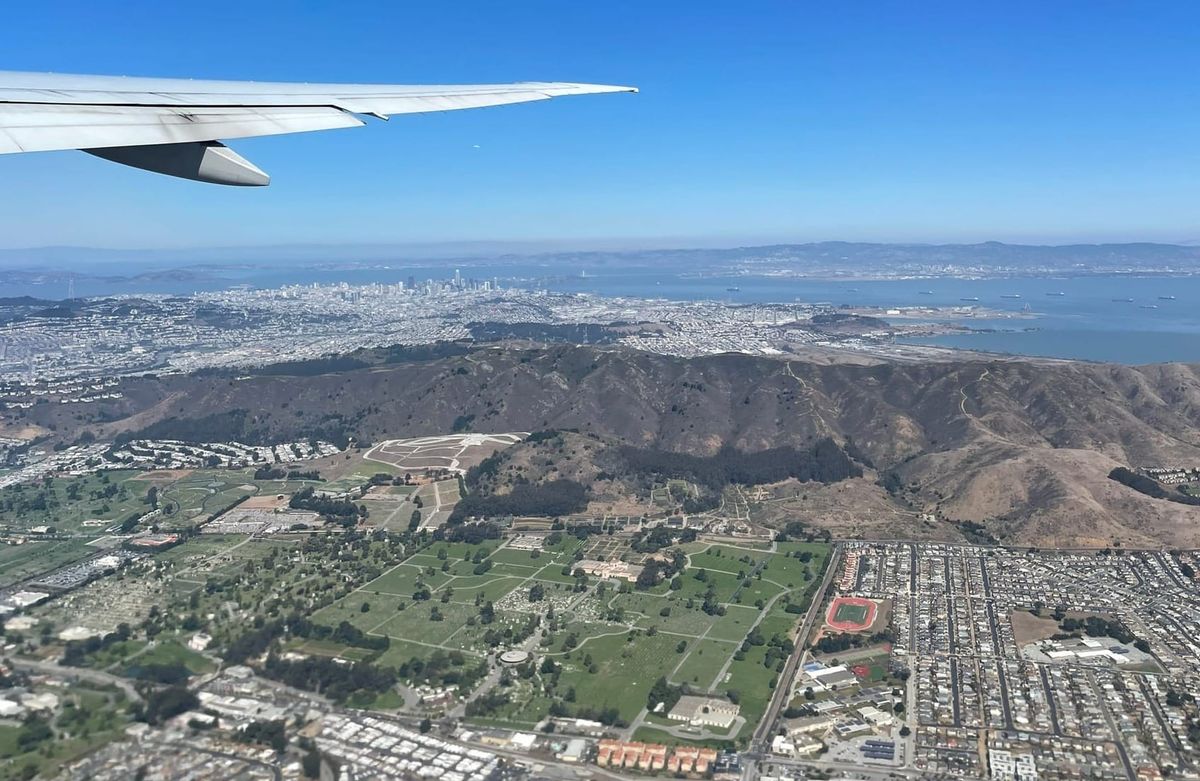 An aerial bird’s-eye view from an airplane window showing a city nestled between a mountain range and a large lake during takeoff.