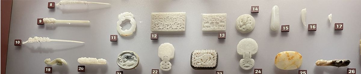 A close-up of ancient, intricately carved jade ornaments displayed on a neutral background, showing fine craftsmanship and structural detail.