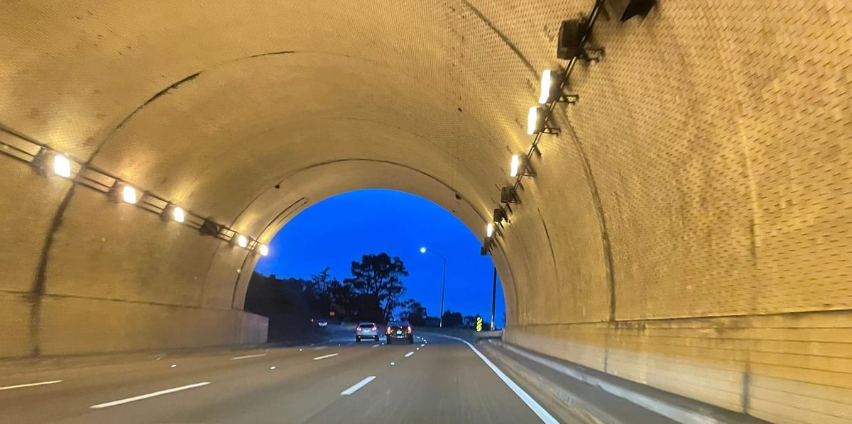 Perspective from inside a tunnel looking toward a bright, circular exit that reveals a night sky and a glowing moon.