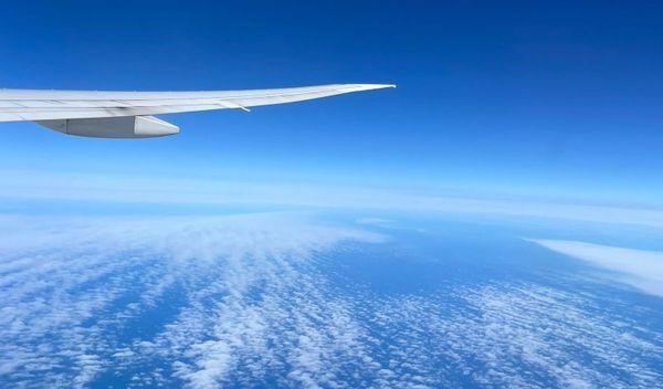 View from an airplane window showing the wing over a dense layer of white clouds.