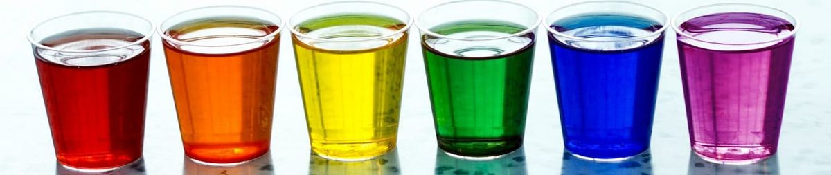 A row of six shot glasses full of coloured liquid in rainbow order, red orange yellow green blue violet.