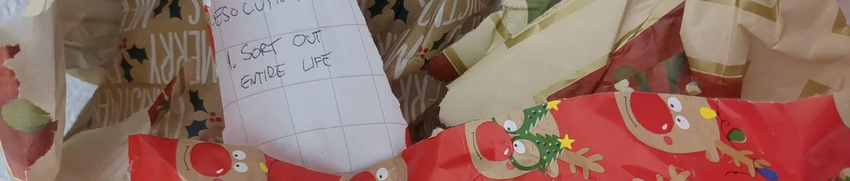 A pile of torn and crumpled Christmas wrapping paper. On the back of one scrap is writing saying "Resolutions: 1. Sort out entire life".