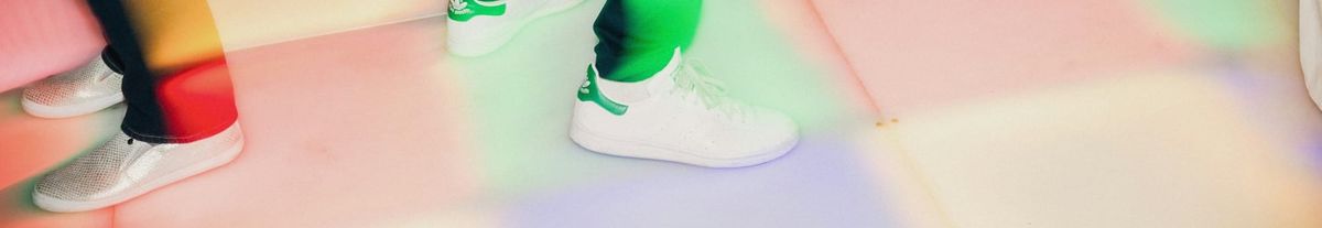 Feet in trainers on a multicoloured dance floor.