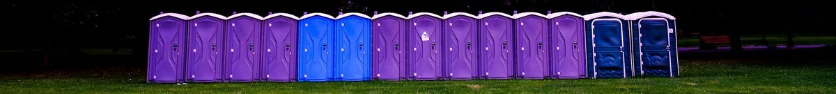 A row of portable toilets on a grassy field.