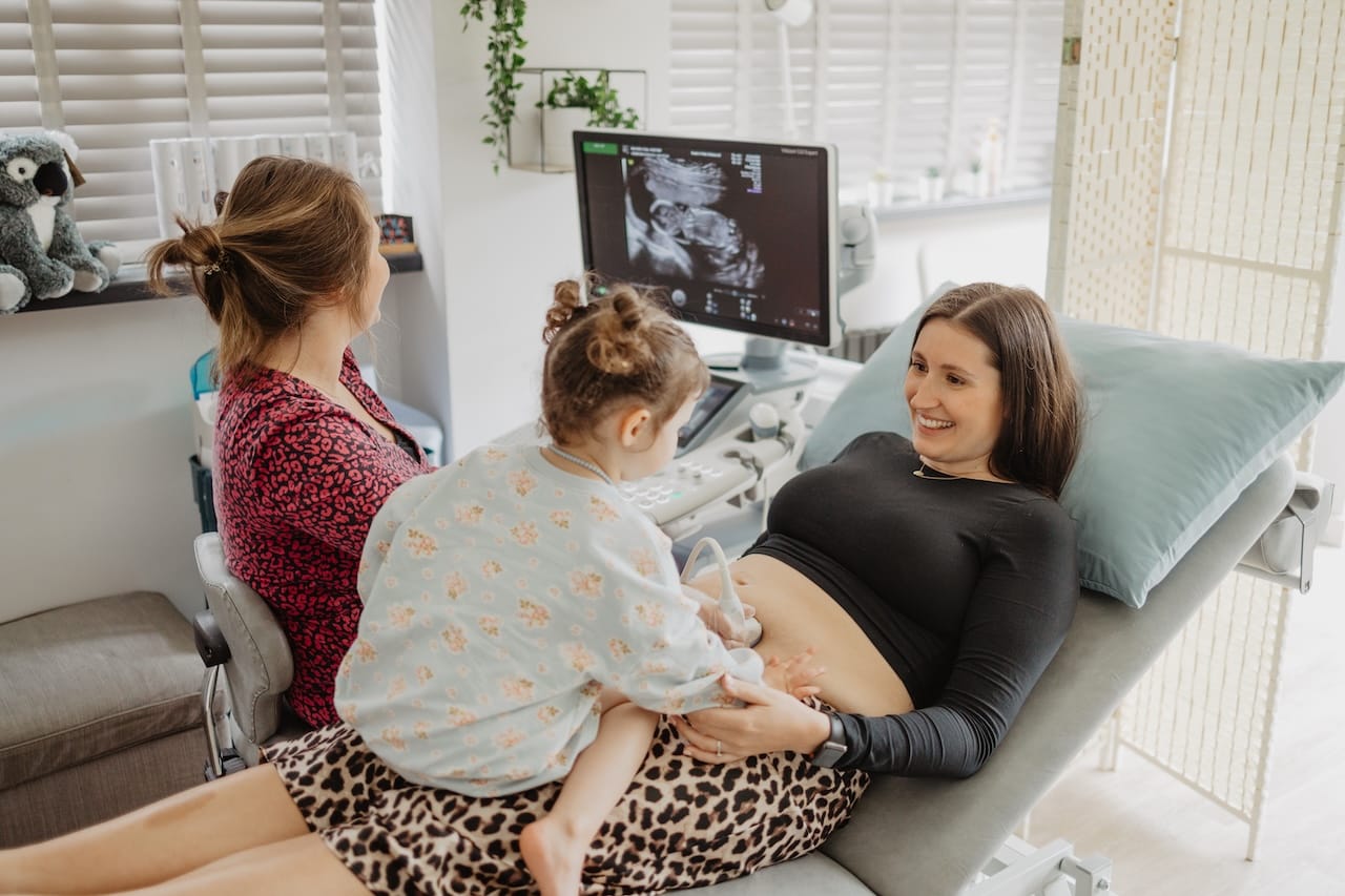 A lady having a pregnancy scan with her daughter on her lap at Sneak-A-Peek Ultrasound.