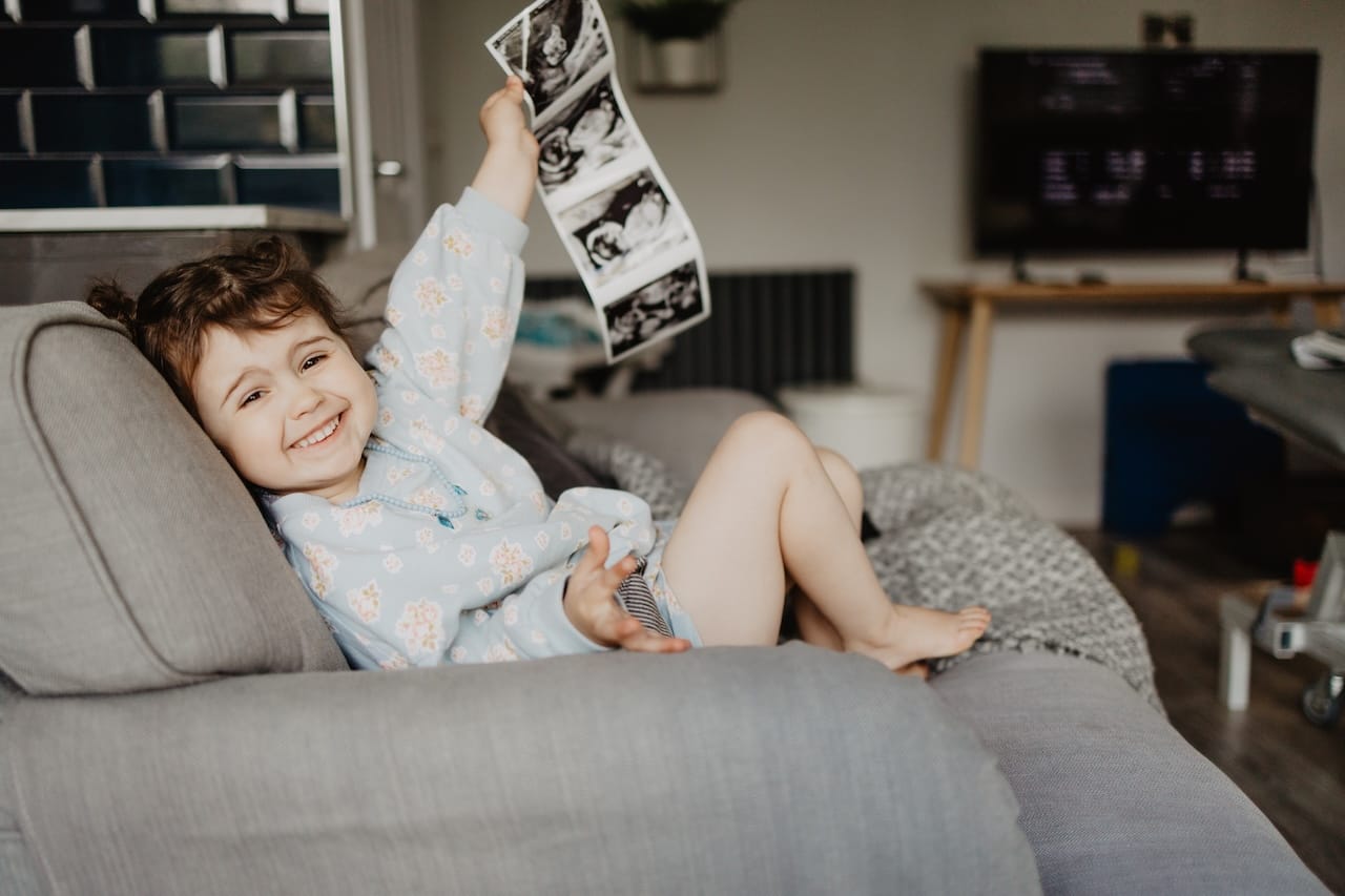 A happy child holding scan pictures of her sibling at a Sneak-A-Peek Ultrasound pregnancy scan.
