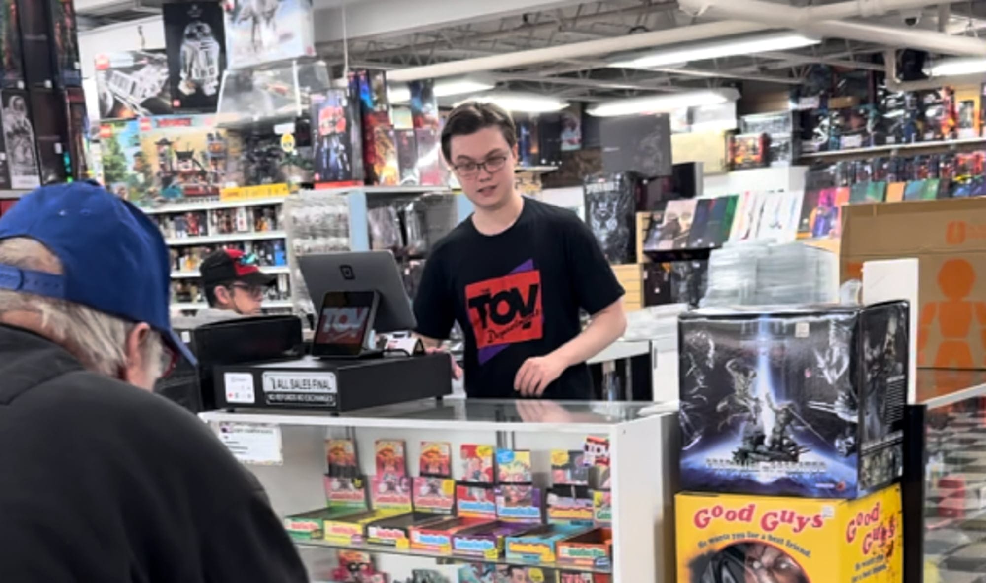 Toy Department employee wearing the branded tee behind the register.