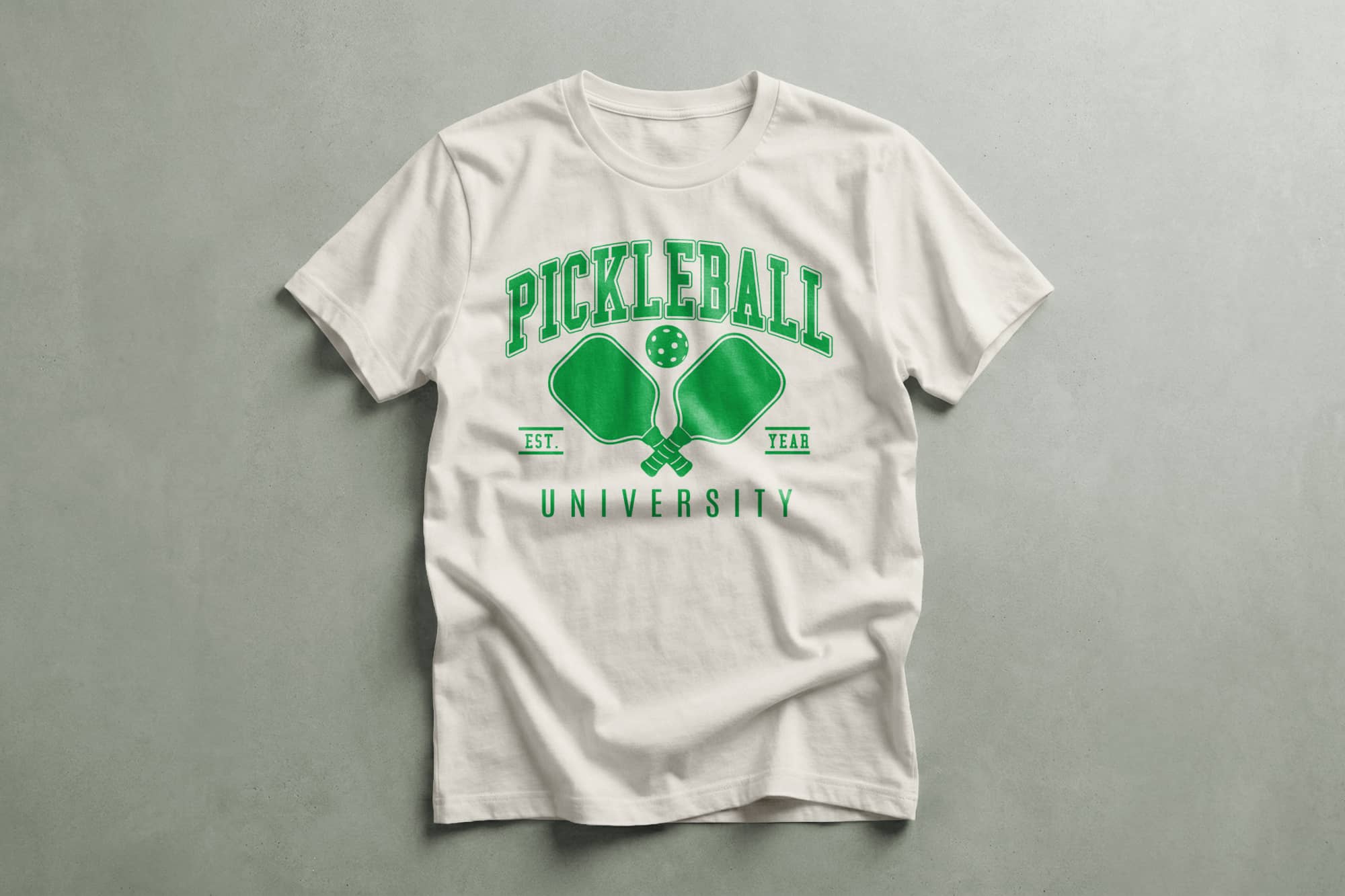 White T-shirt with "Pickleball University" in green text. Features two paddles and a ball graphic. Casual and sporty tone.