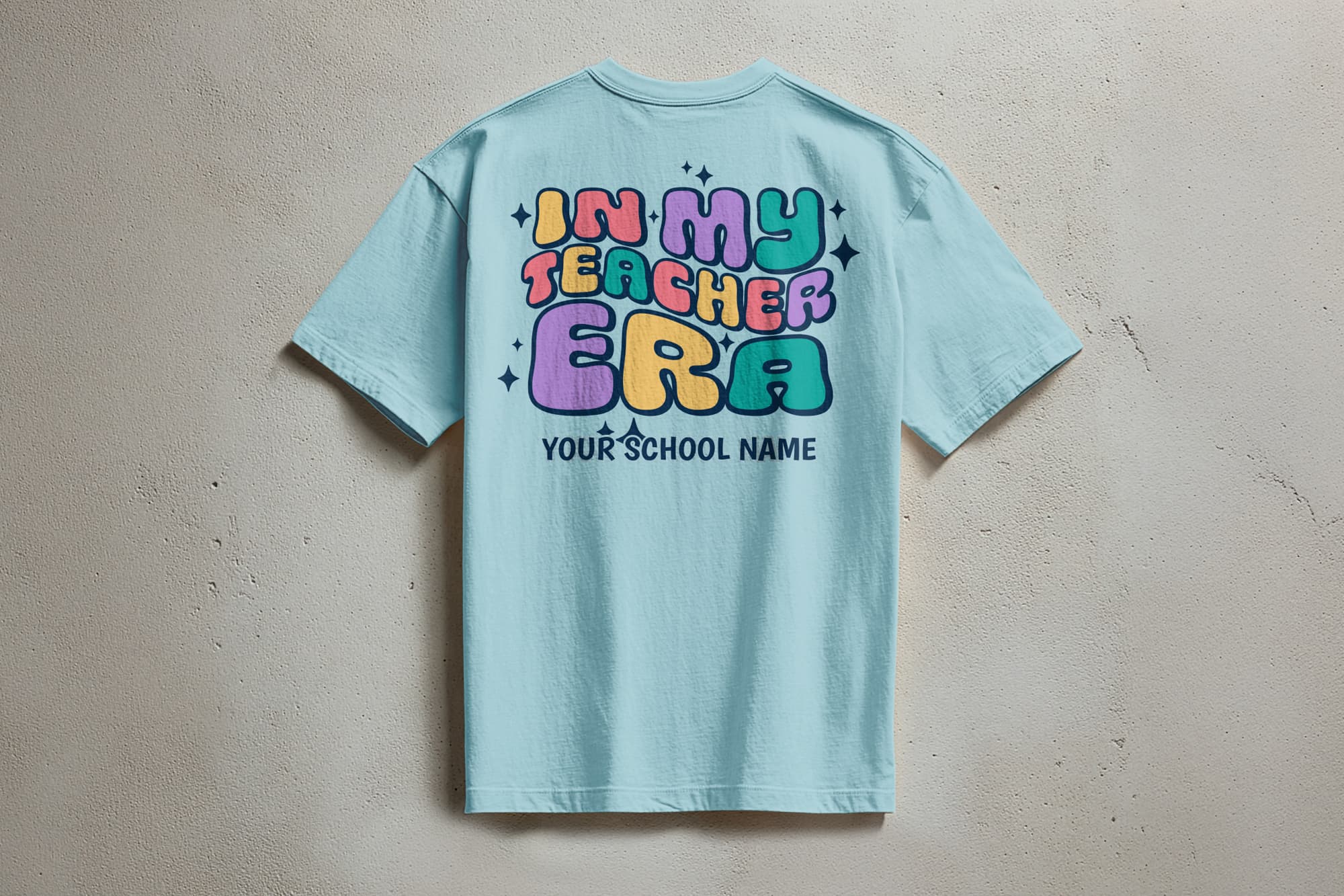 Light blue T-shirt with colorful, playful text: "In My Teacher Era" and "Your School Name" below. The design conveys a fun, vibrant tone.