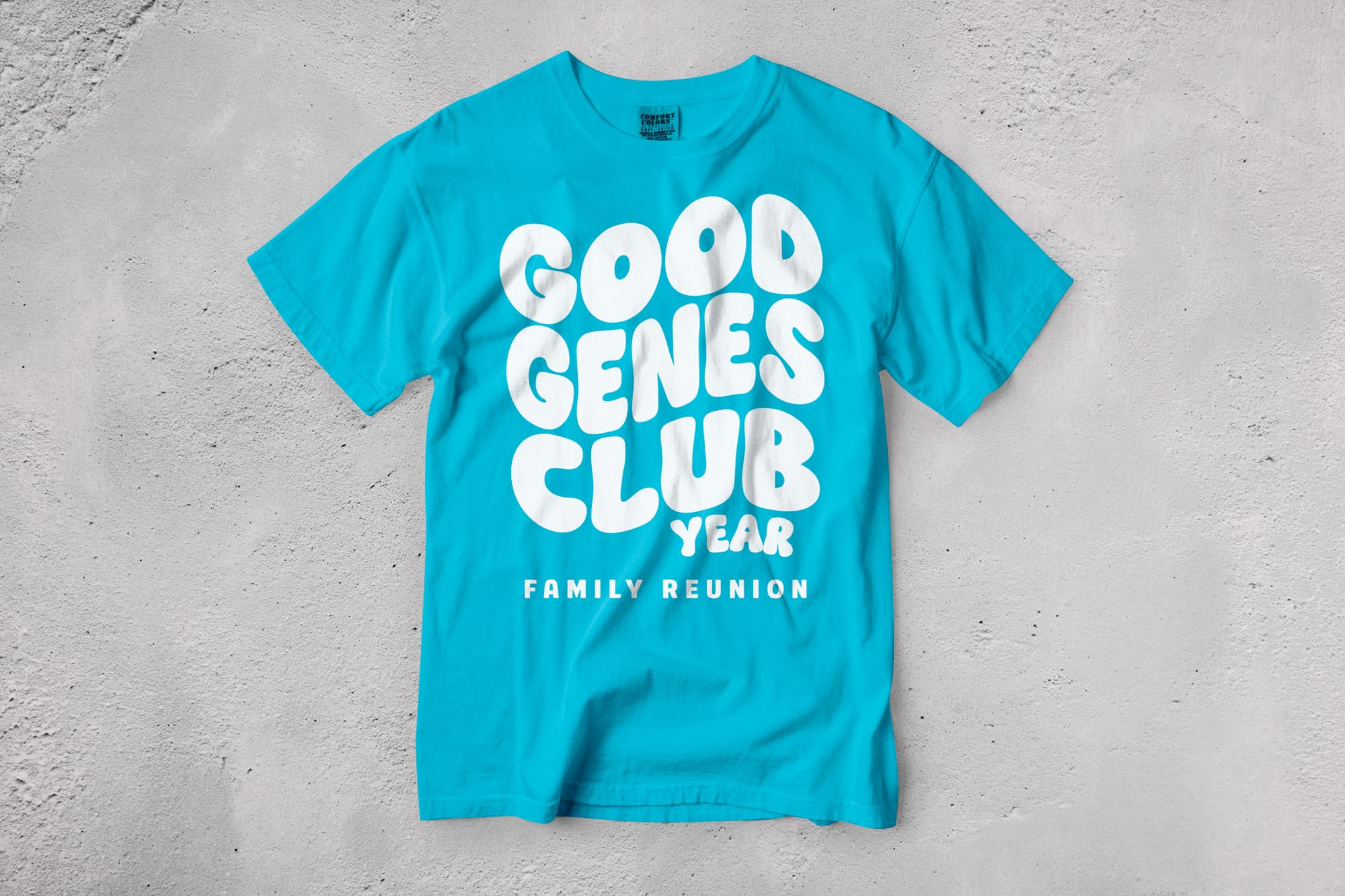 Turquoise T-shirt with bold white text "Good Genes Club Year" and "Family Reunion" set against a textured gray background, giving a lively feel.