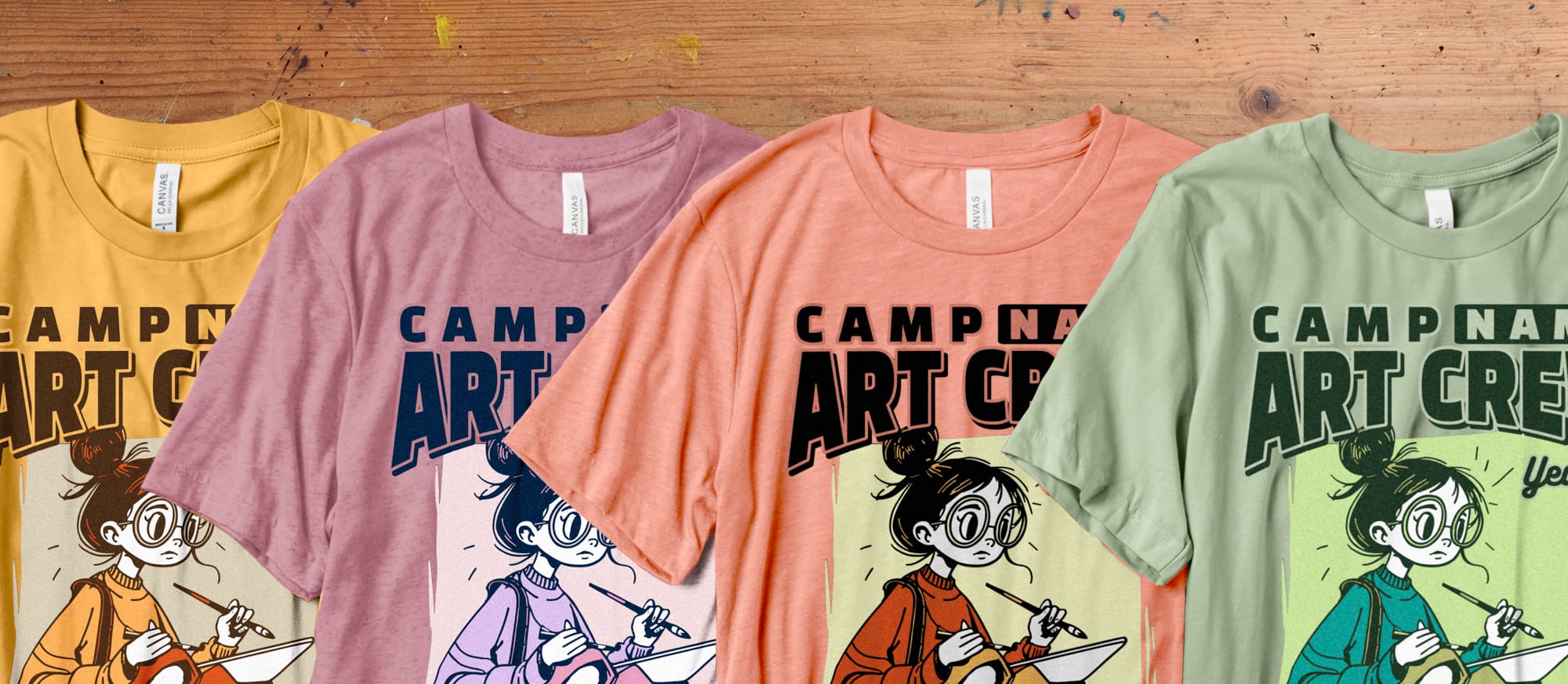 Four colorful t-shirts with a cartoon artist design and “Camp Name Art Crew” text, arranged on a wooden table. Each shirt is in a different color.