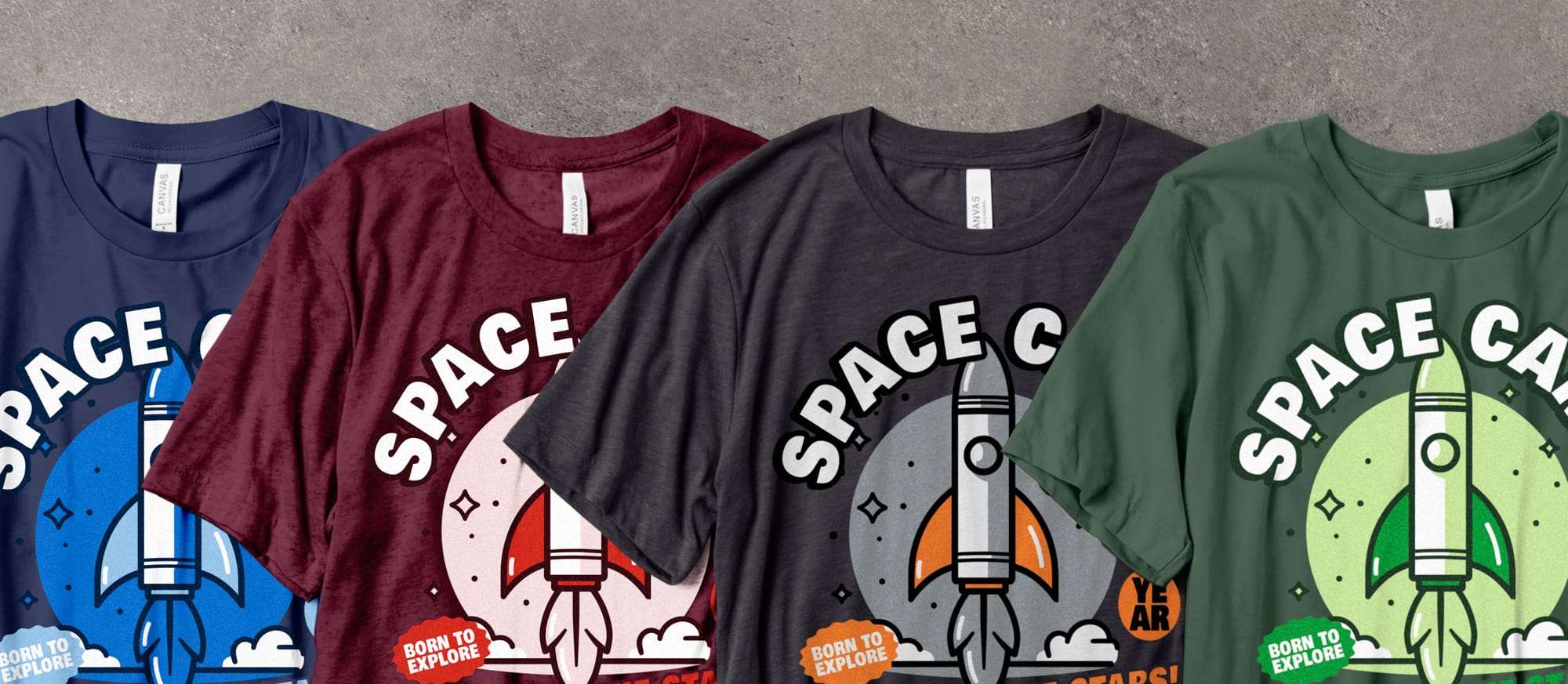 Four colorful T-shirts with space-themed rocket designs labeled "Space Camp." Colors are blue, red, gray, and green, with the phrase "Born to Explore."