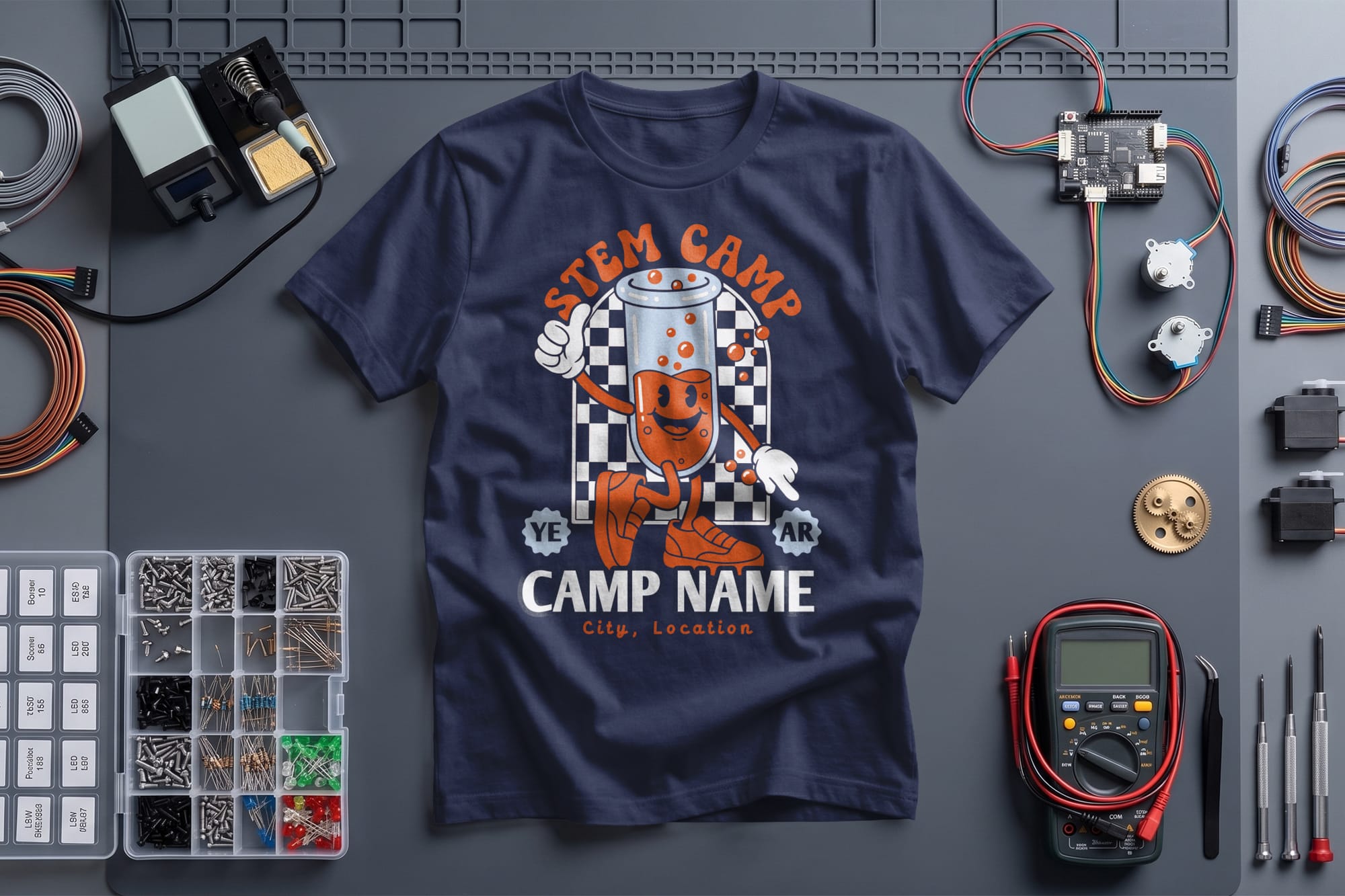 Navy blue STEM camp T-shirt featuring a cartoon robot and checkered background is surrounded by electronics components, tools, and circuit boards.