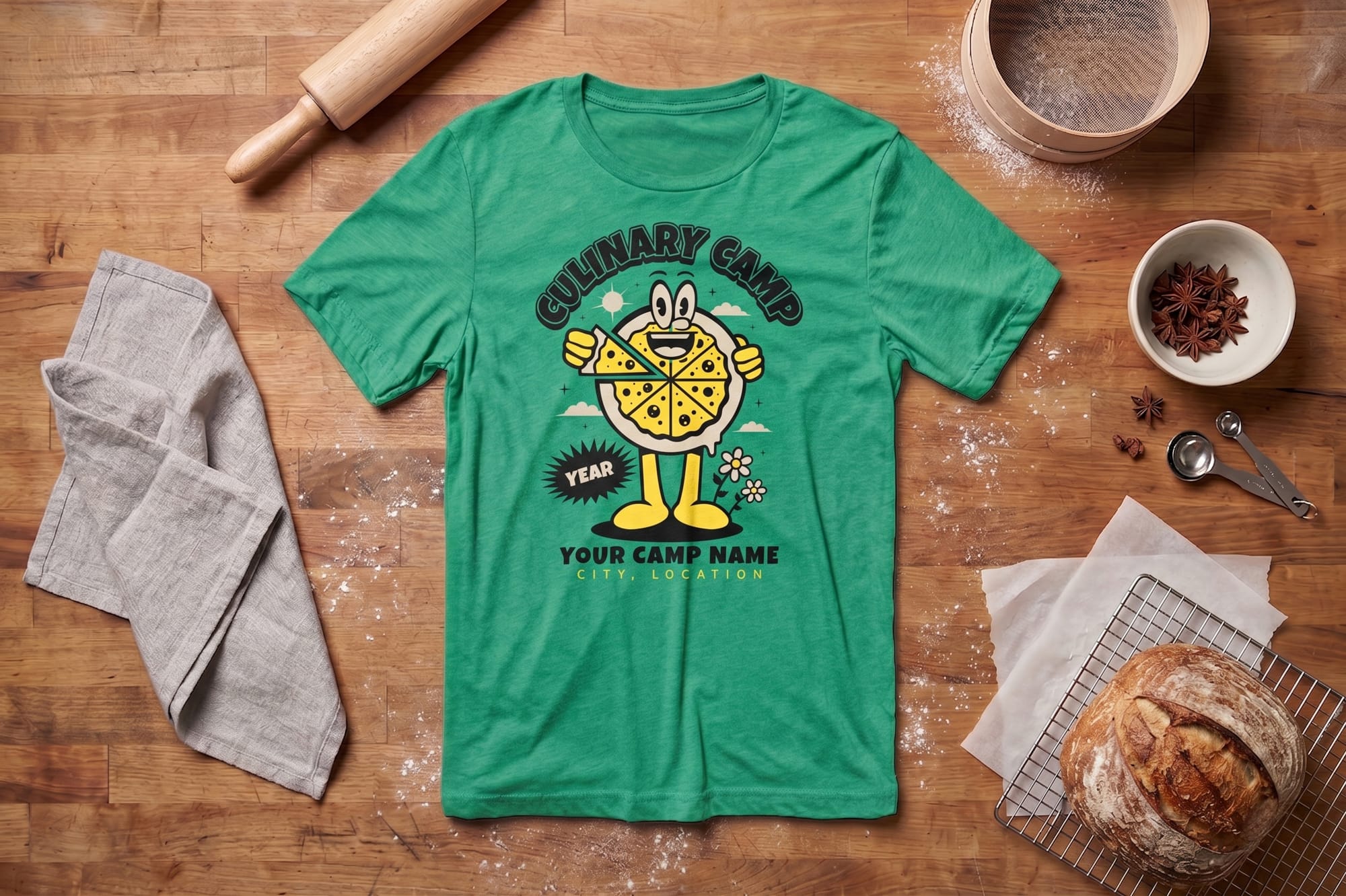 Green t-shirt with a cartoon pizza and text "Culinary Camp" on wooden table. Surrounding items: rolling pin, gray towel, spices, bread, and baking tools.