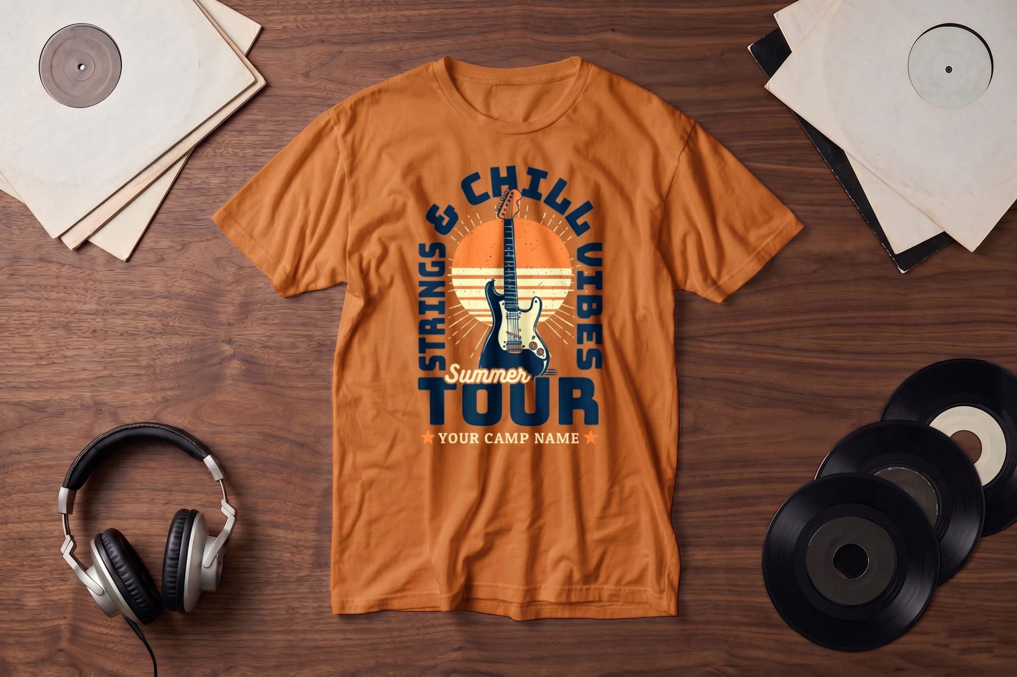 Orange T-shirt on a wooden surface with a guitar and "Strings & Chill Vibes Summer Tour" design. Surrounding items include headphones and vinyl records, evoking a retro music vibe.