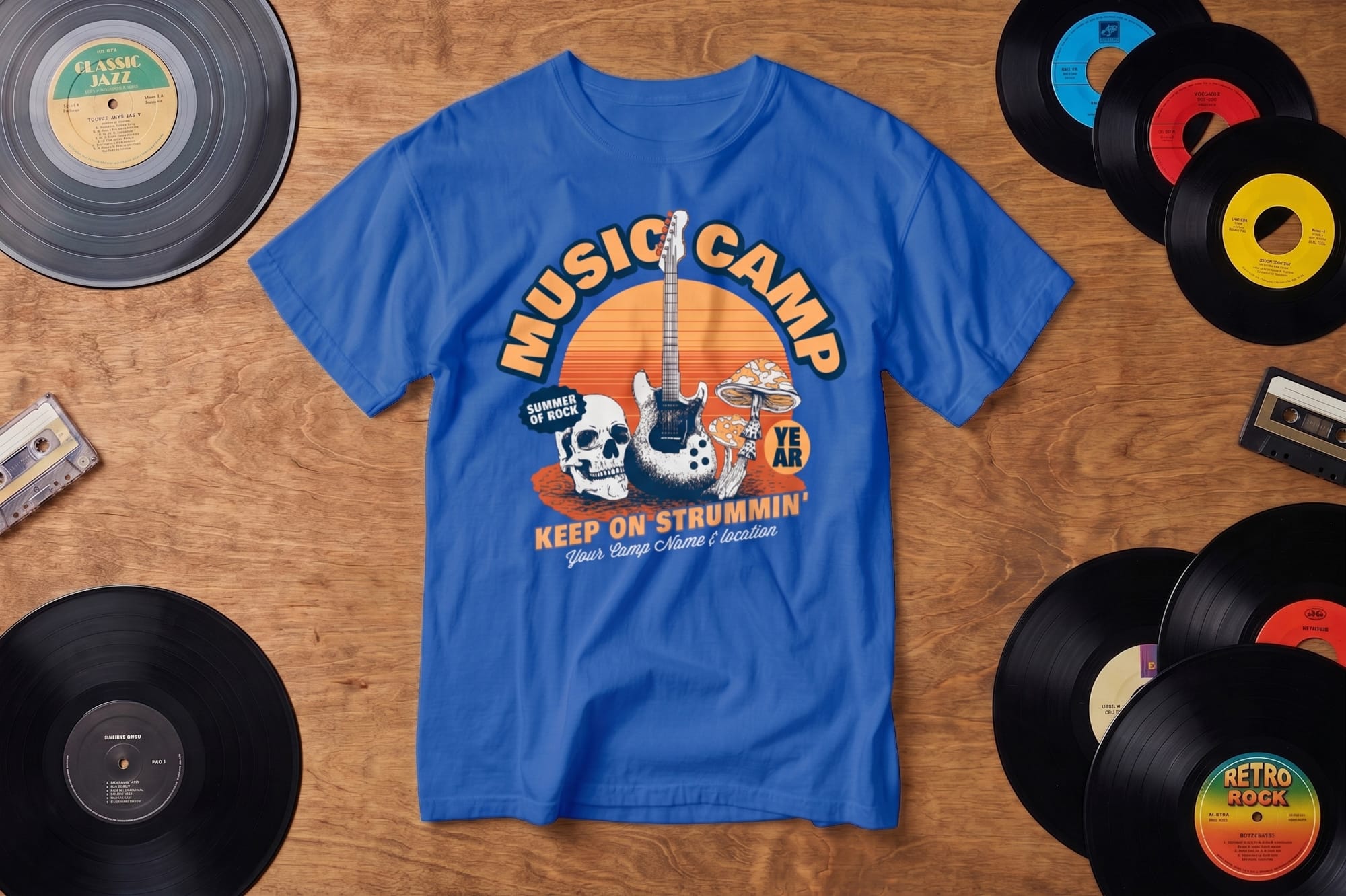 Blue T-shirt with "Music Camp" and a guitar design is centered on a wooden surface, surrounded by vinyl records and cassette tapes, evoking a retro vibe.