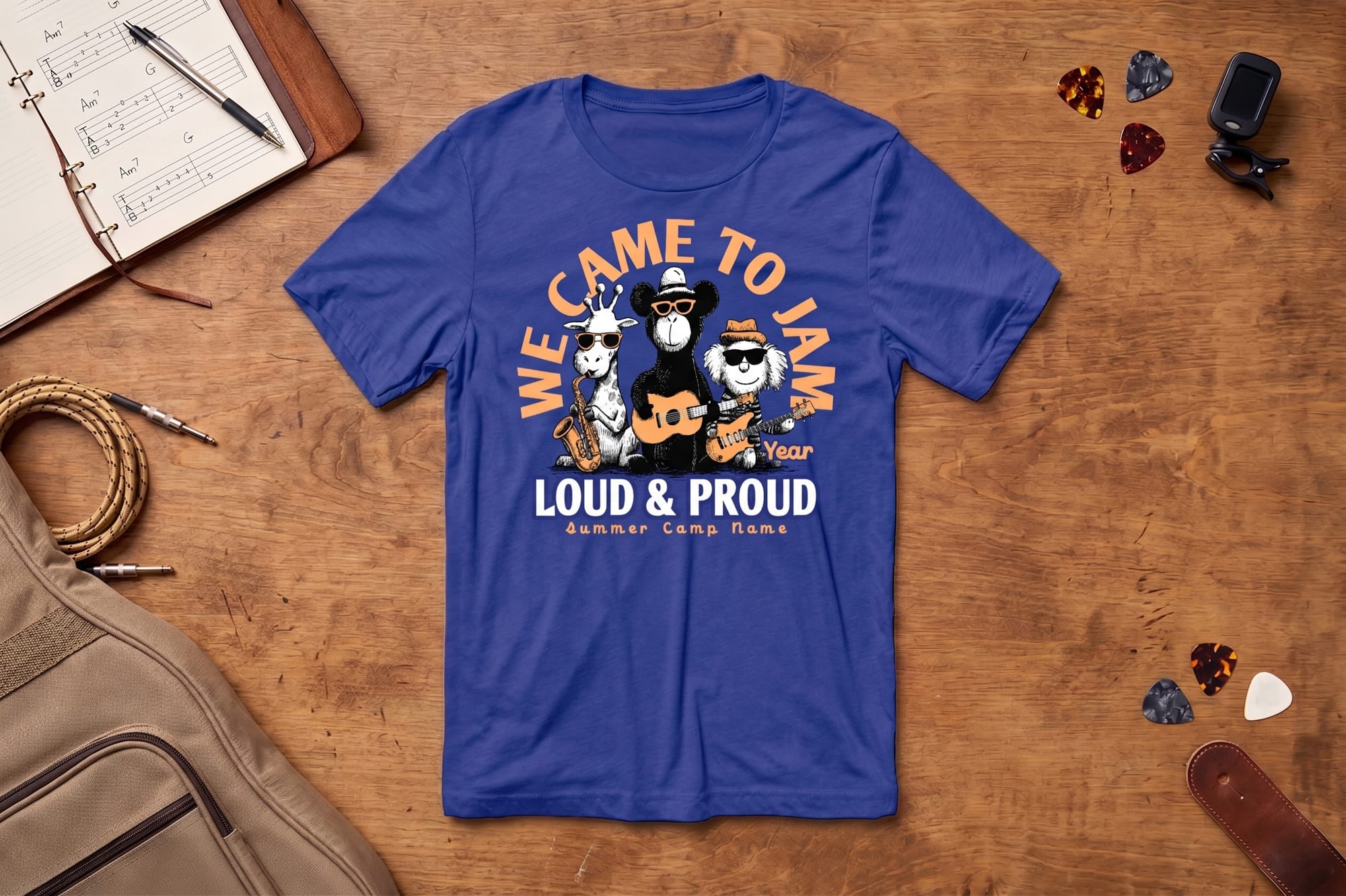 Blue T-shirt on a wooden table with cartoon animals playing instruments. Text reads "We Came To Jam, Loud & Proud, Summer Camp Name." Vibrant and fun.