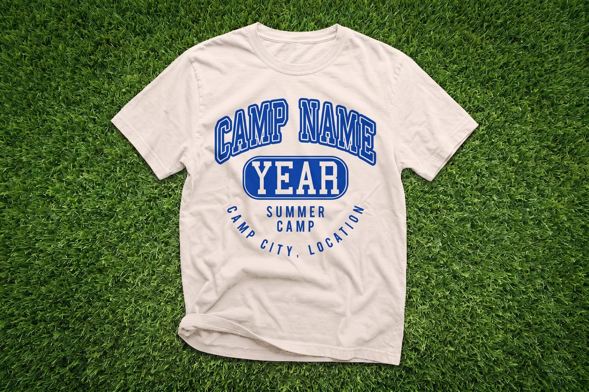 A white T-shirt with blue text reading "Camp Name" and "Year" in bold, placed on green grass. It conveys a fun summer camp vibe.