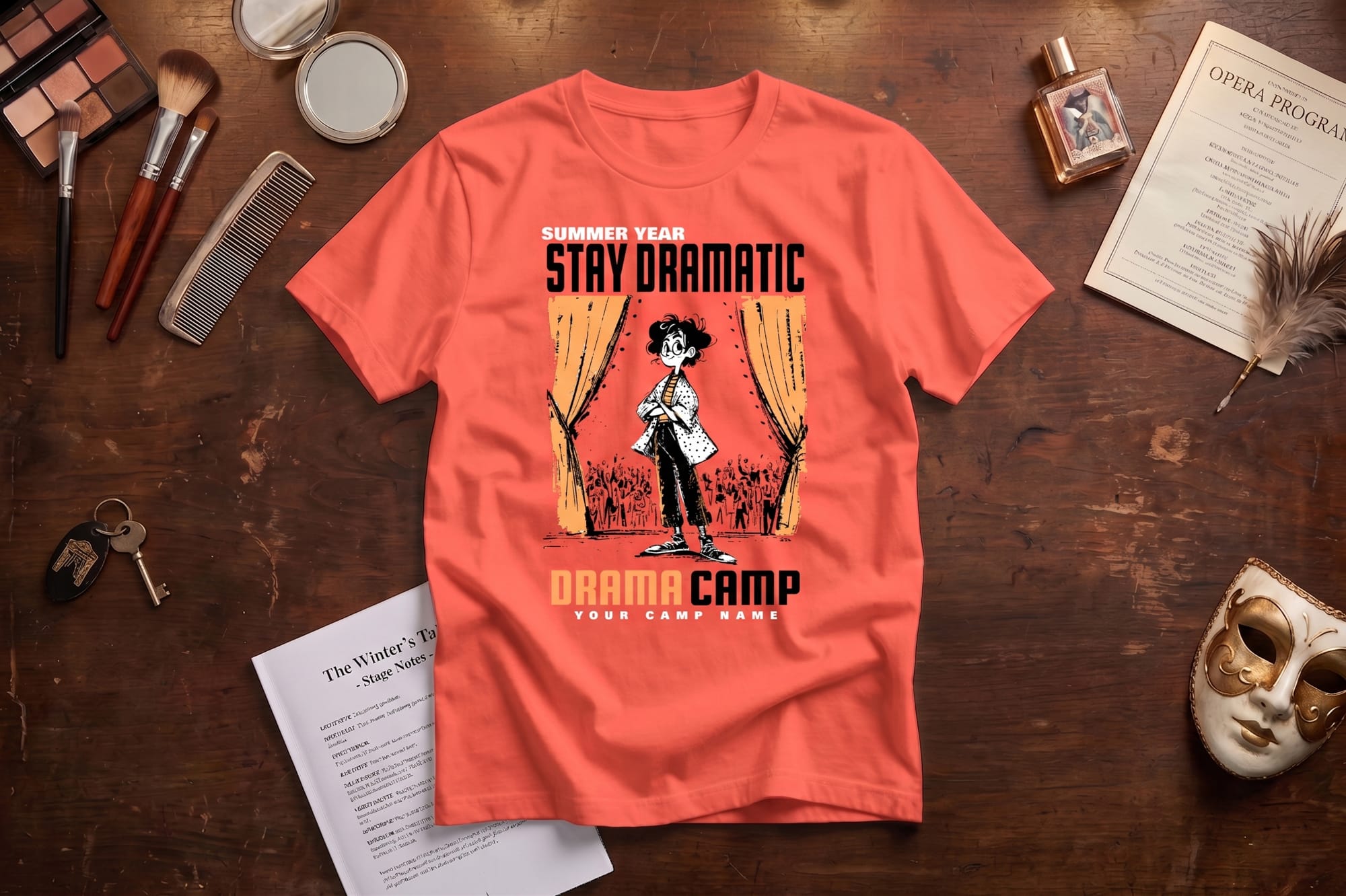 Coral custom-printed drama camp t-shirt with 'Stay Dramatic' graphic of a performer on stage, flatlay styled with theater props