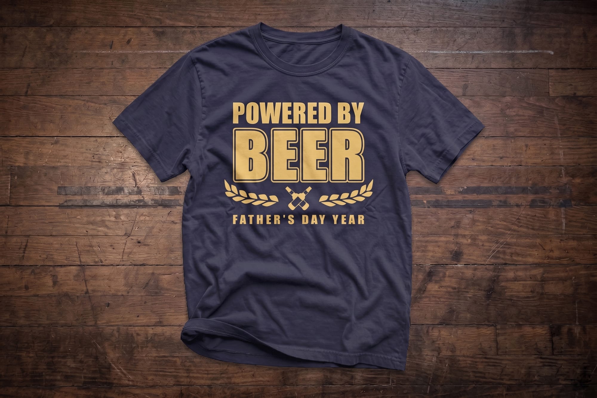 Navy crewneck t-shirt with a gold 'Powered by Beer' custom-printed Father's Day design, flatlay on wood