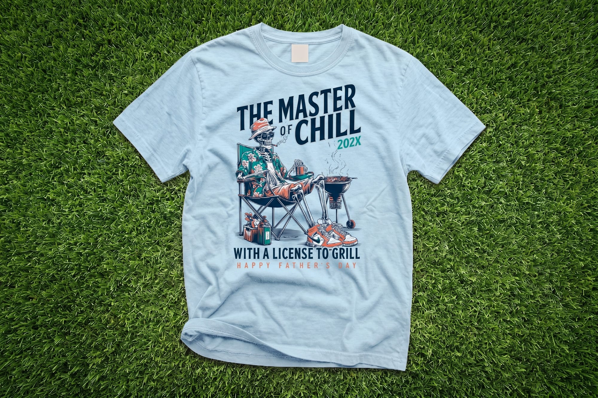 Light blue crewneck tee with a Father's Day skeleton grilling graphic and 'The Master of Chill — License to Grill' text
