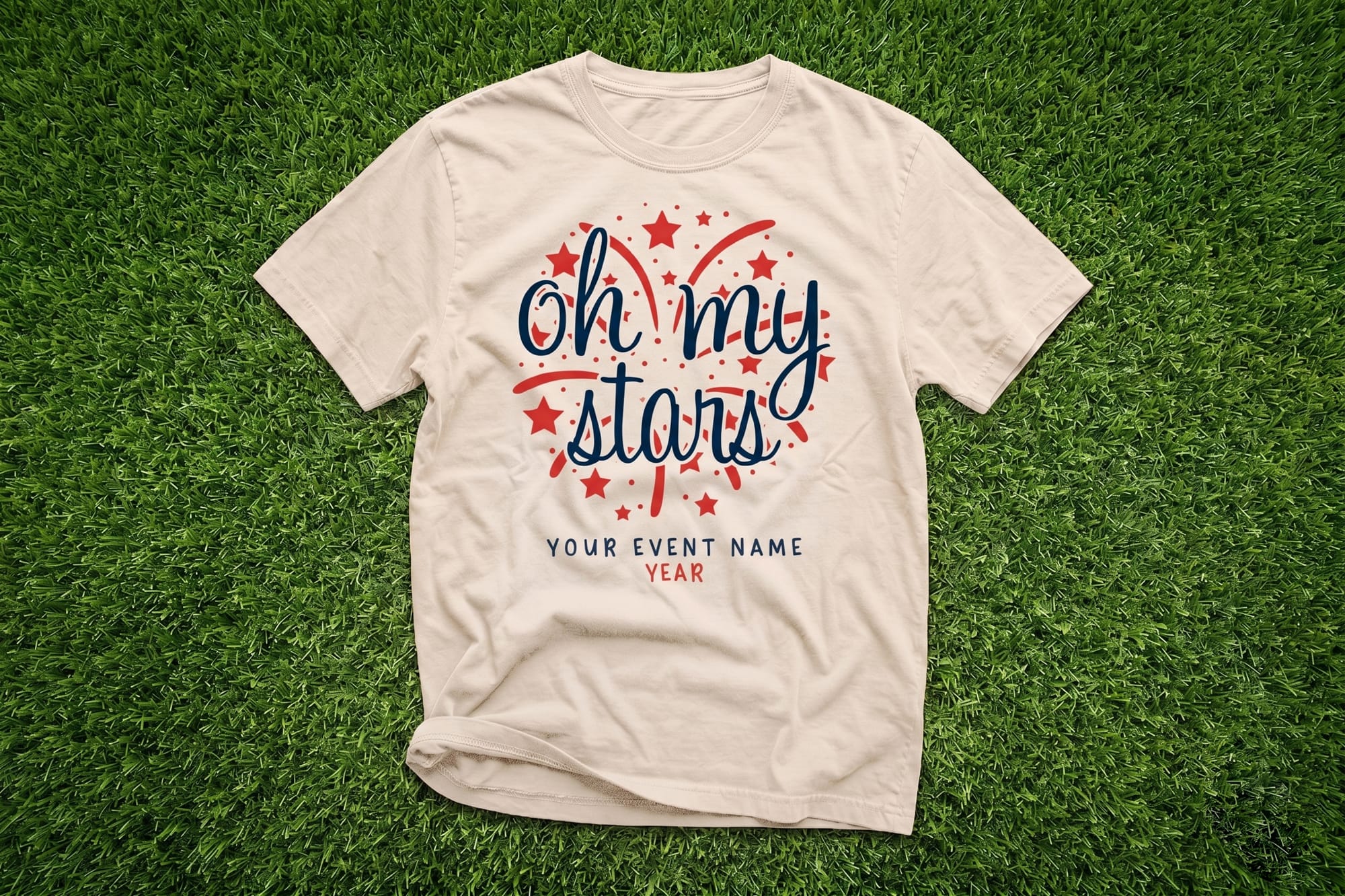Natural crewneck t-shirt with a patriotic 'Oh My Stars' fireworks design in navy and red, laid on grass