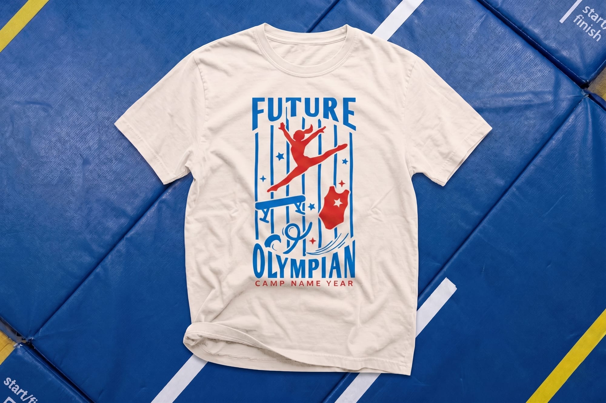 Natural crewneck tee with a red and blue 'Future Olympian' gymnastics camp design, laid flat on blue gym mats