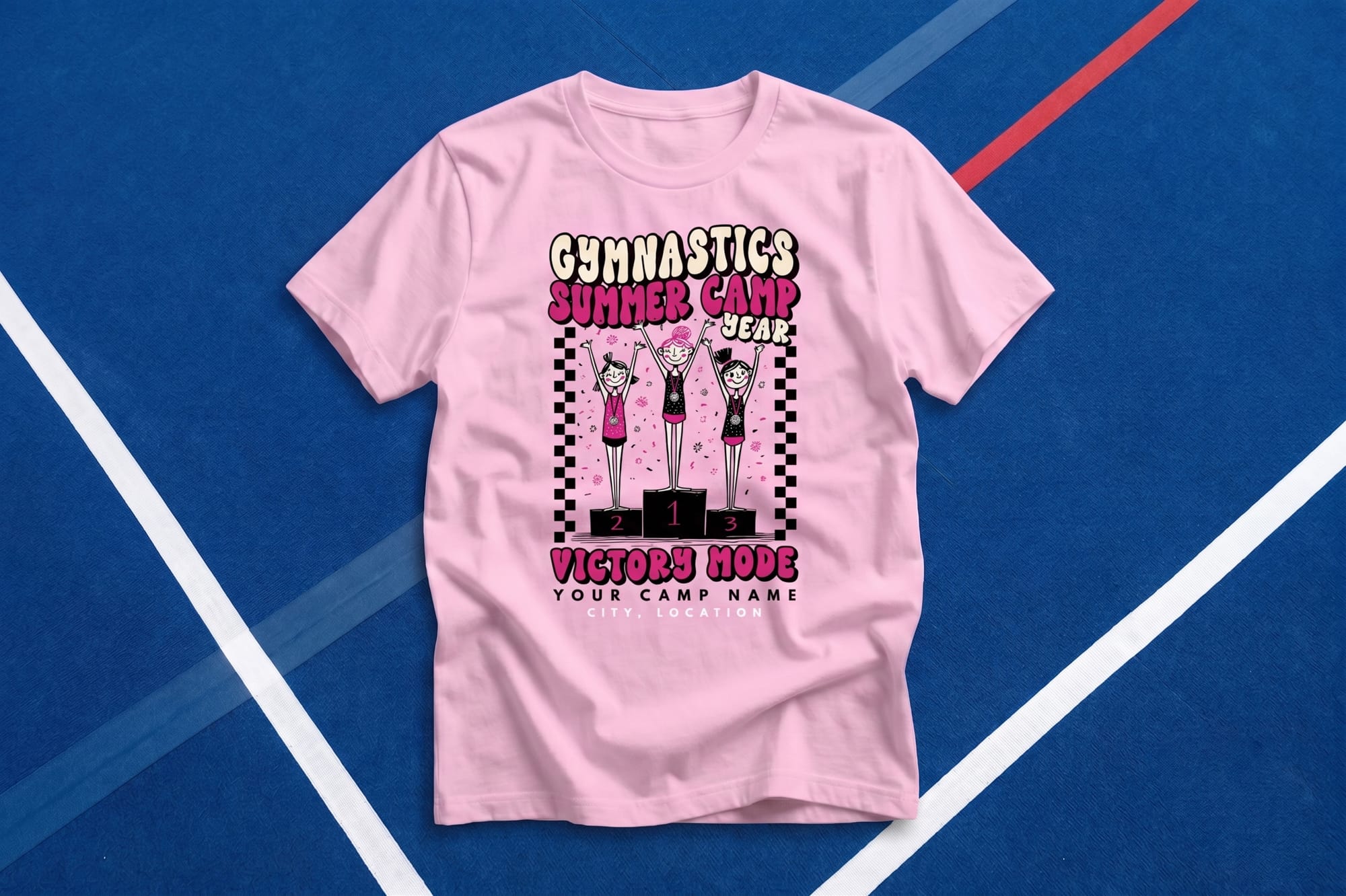 Light pink custom gymnastics summer camp t-shirt with a retro podium illustration and 'Victory Mode' text, shown as a flatlay on a gym floor