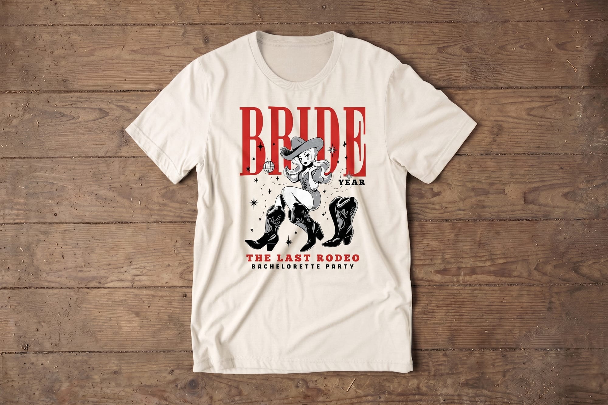 Natural crewneck tee with a retro cowgirl illustration and red 'Bride — The Last Rodeo Bachelorette Party' screen-printed design