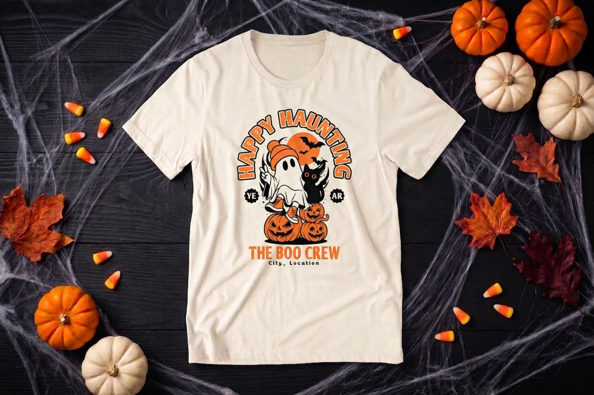 Cream t-shirt template with a cartoon ghost in a beanie, a black cat, jack-o'-lanterns, and editable crew name and location