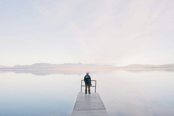 Photographer Wearing Jacket Standing on Wooden Docks Leading to Body of Water