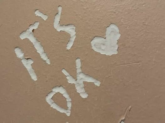 the words "it's ok" and a heart carved into a tan wall