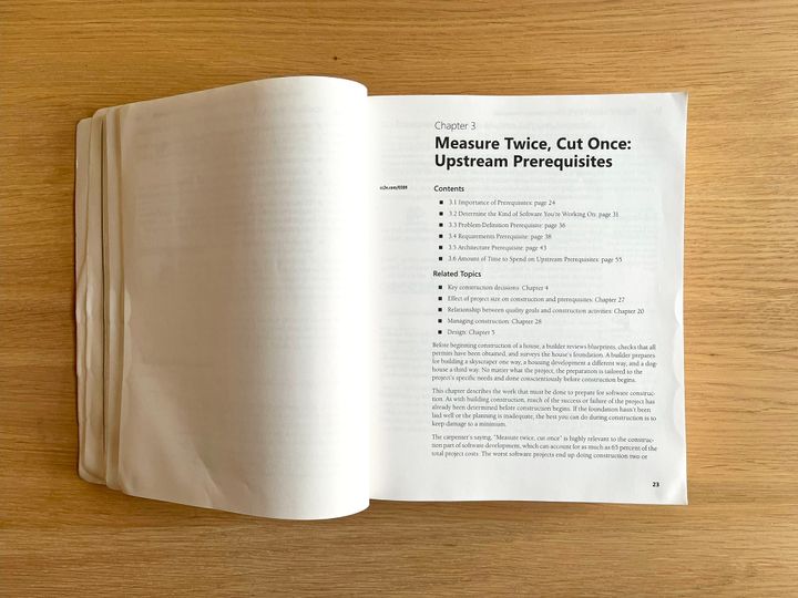 "Code Complete" by Steve McConnell lying on a wooden table, opened to Chapter 3.