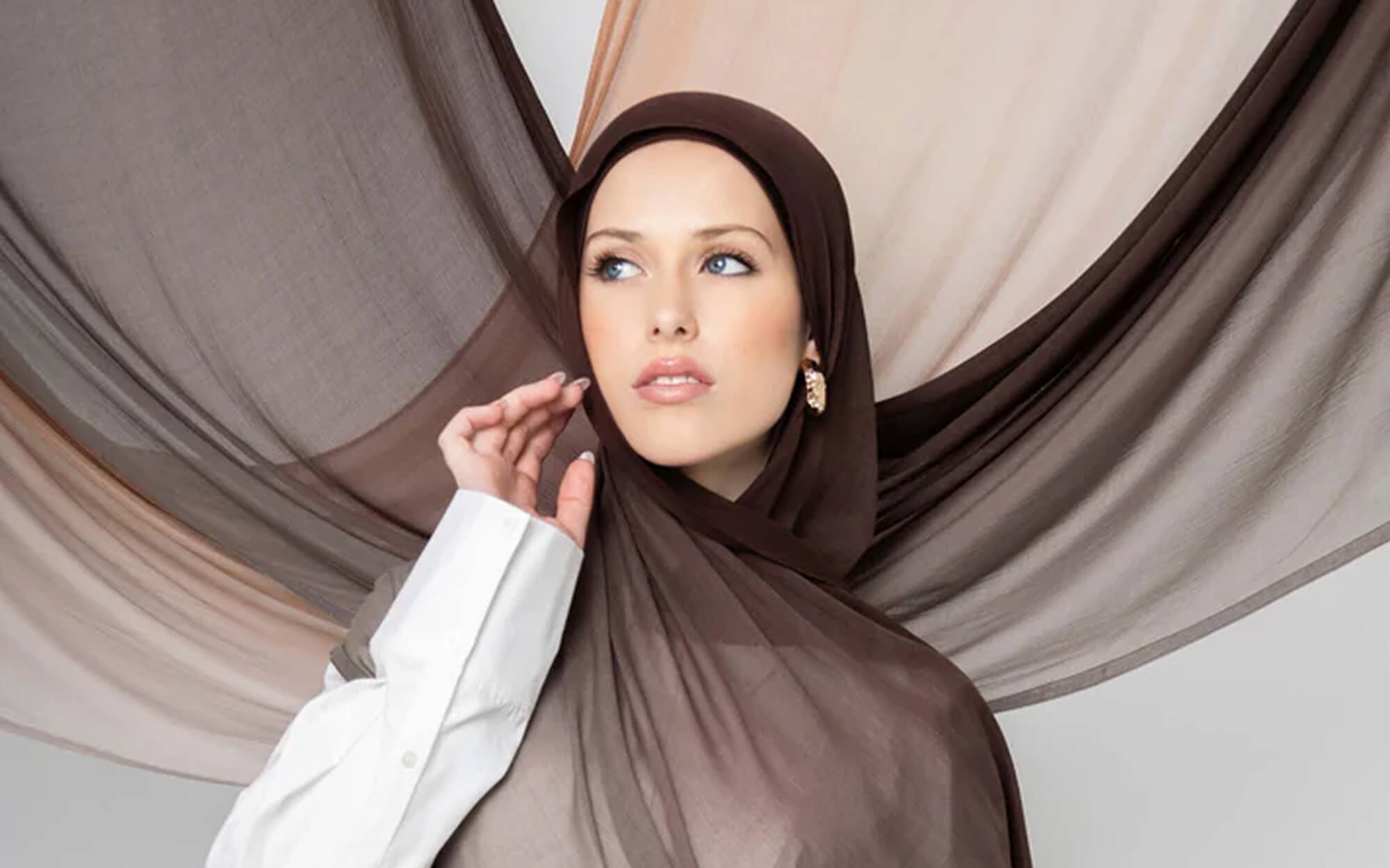 A woman wearing a sheer ombré hijab that fades from dark brown to soft taupe, draped gracefully around her shoulders.